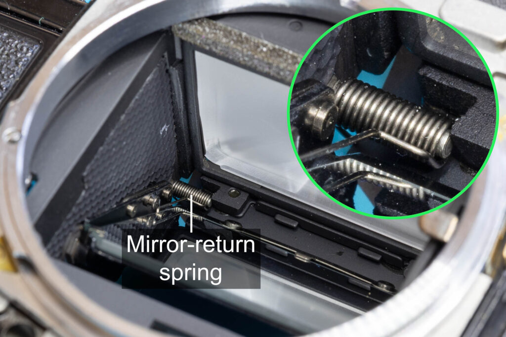 Canon A-1: Mirror-return spring placed in the upper left corner of the mirror box, secured by screw pin