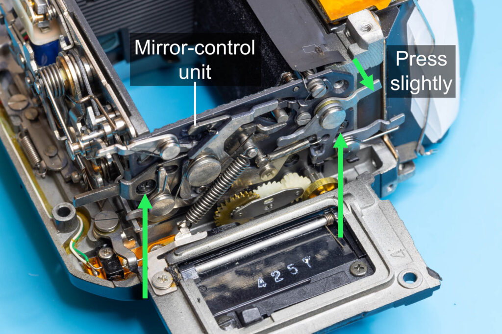 Canon A-1: Loosen the screws by half a turn and press the mirror-control unit slightly to the right